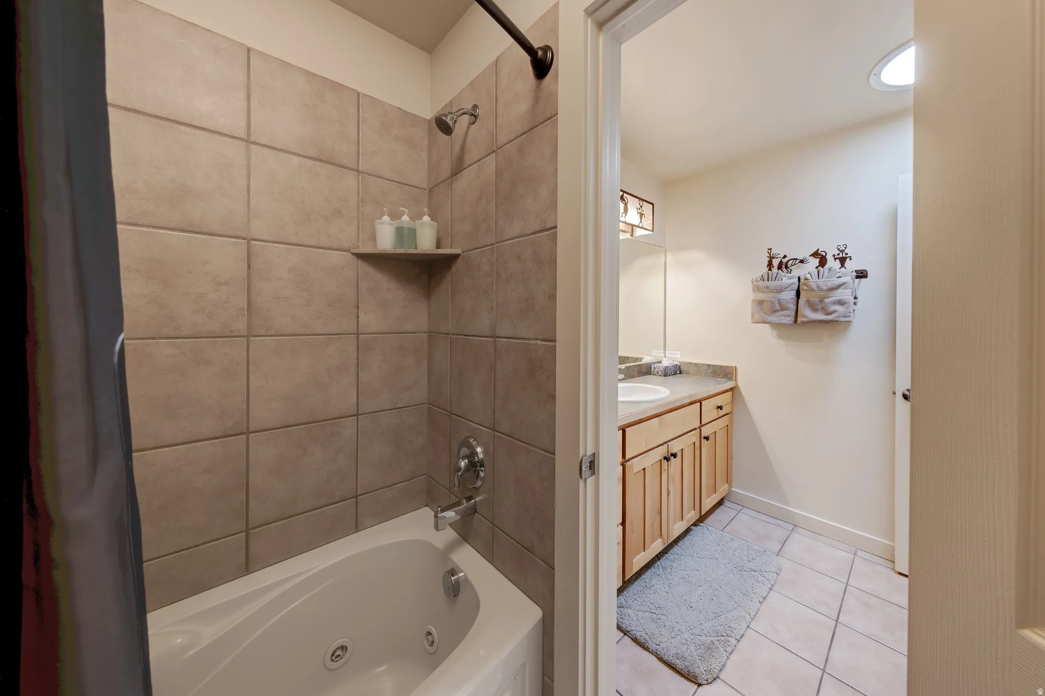 Jetted tub with tile surround, wood cabinetry with a countertop, recessed lighting, and a circular skylight