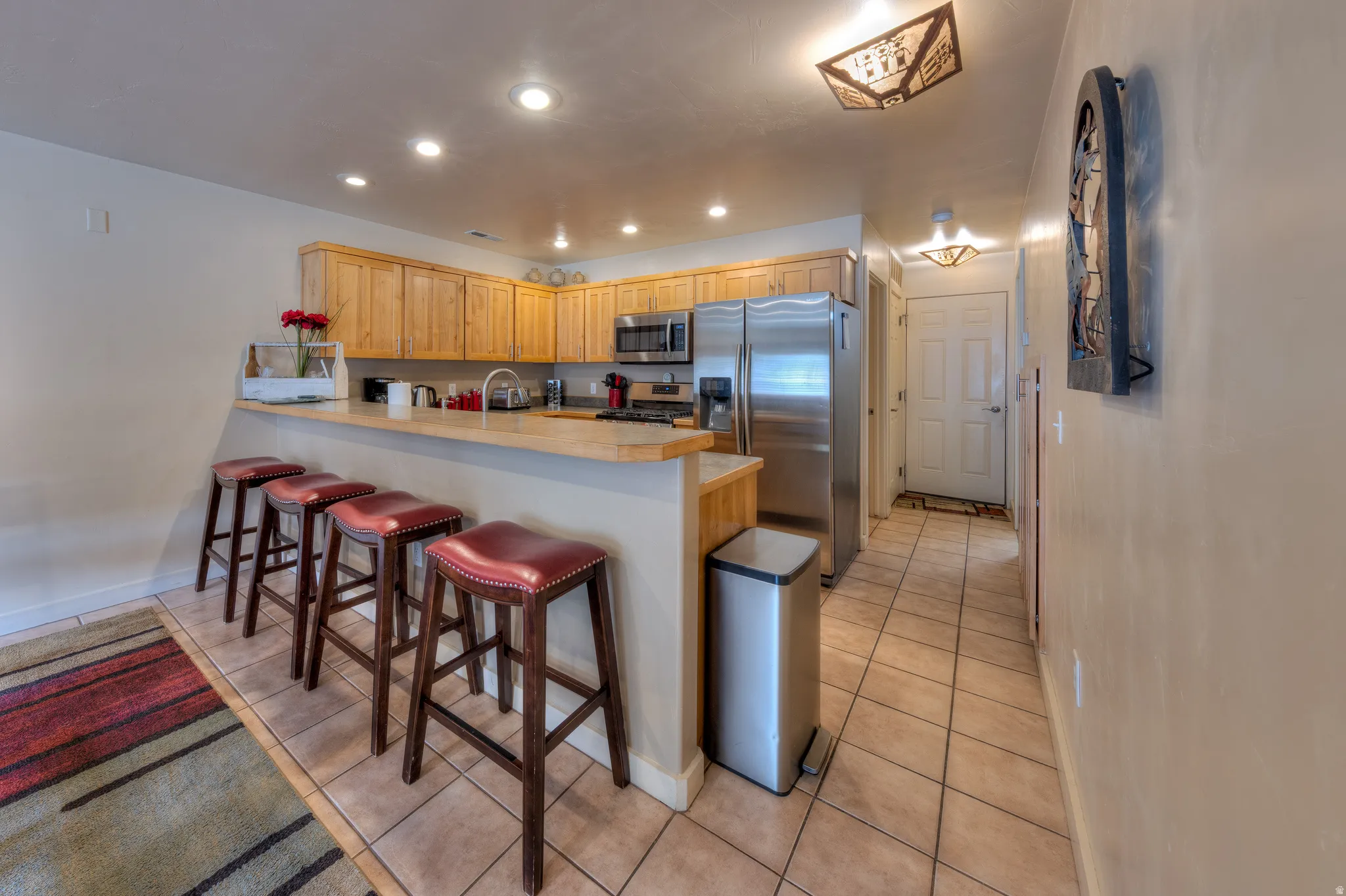 Kitchen featuring wood cabinetry, stainless steel appliances, a breakfast bar, recessed lighting, and tile flooring