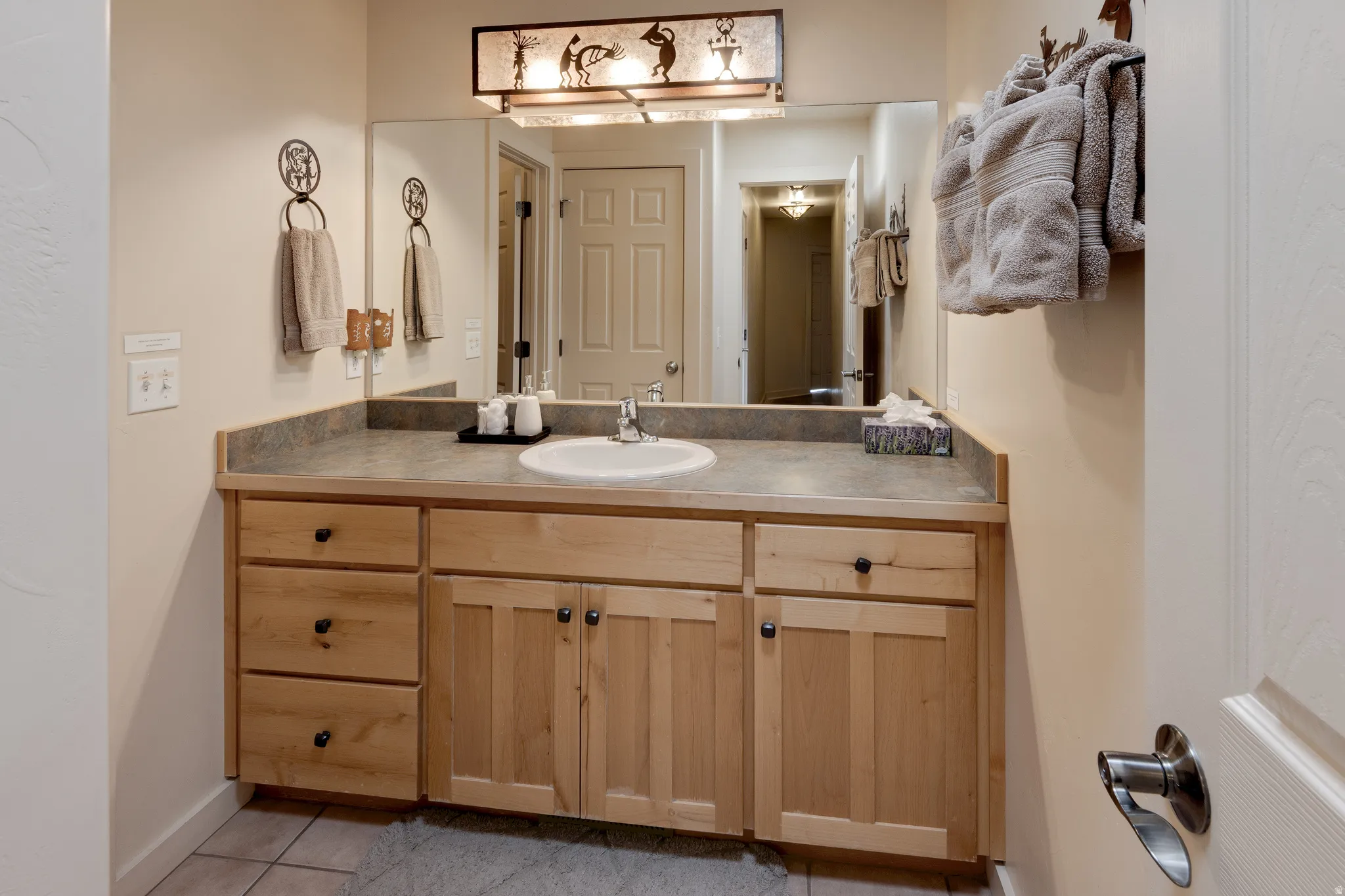 Light-toned vanity with wood-finish cabinetry, a single basin sink, and a dark countertop