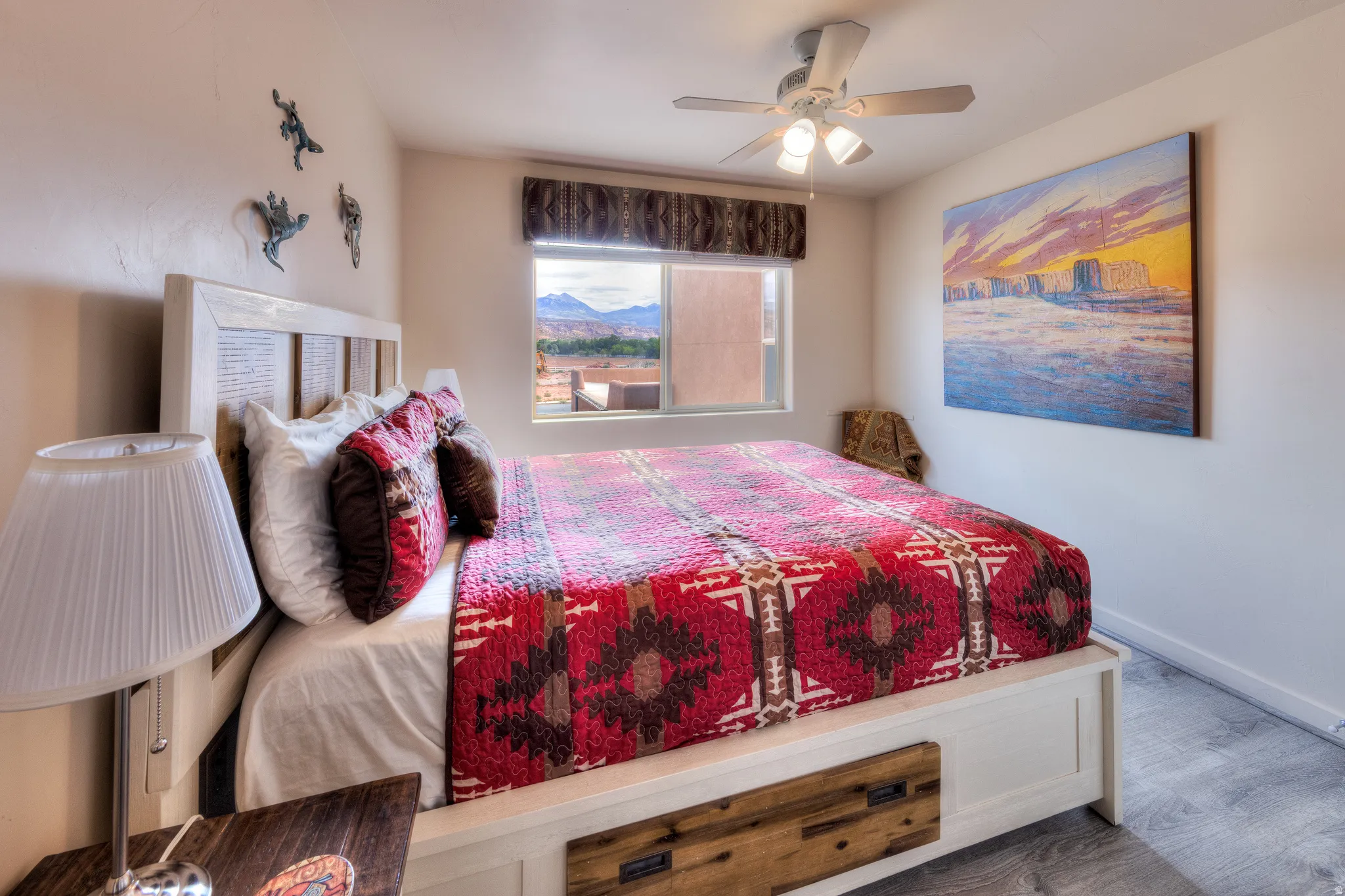 Built-in bed frame with integrated storage drawers, window with mountain scenery, ceiling fan with integrated lighting, wood-finish flooring, and neutral wall paint
