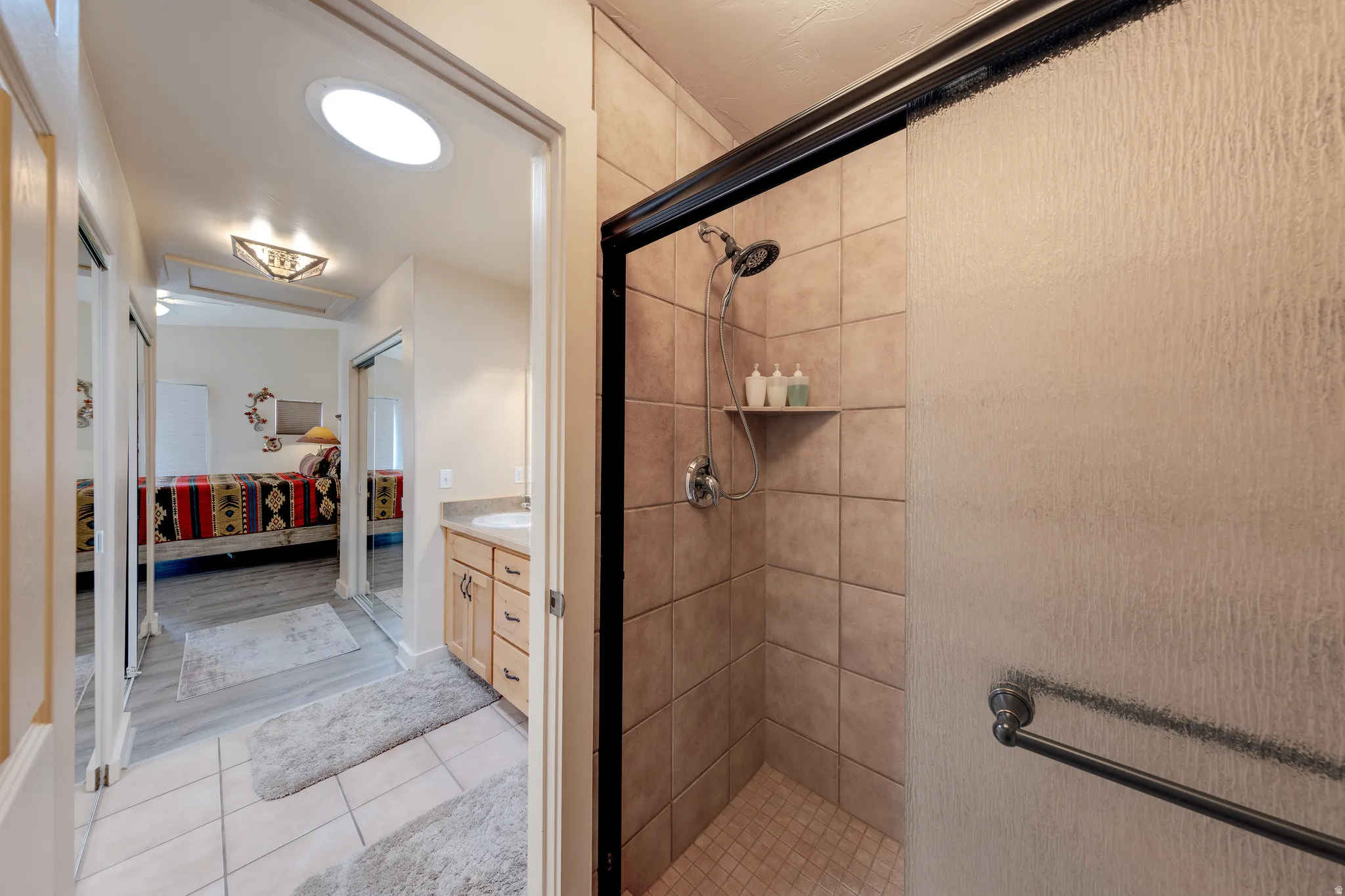 Tiled shower with a sliding glass door, a skylight, a wood-finish vanity with a countertop sink, and wood-finish flooring