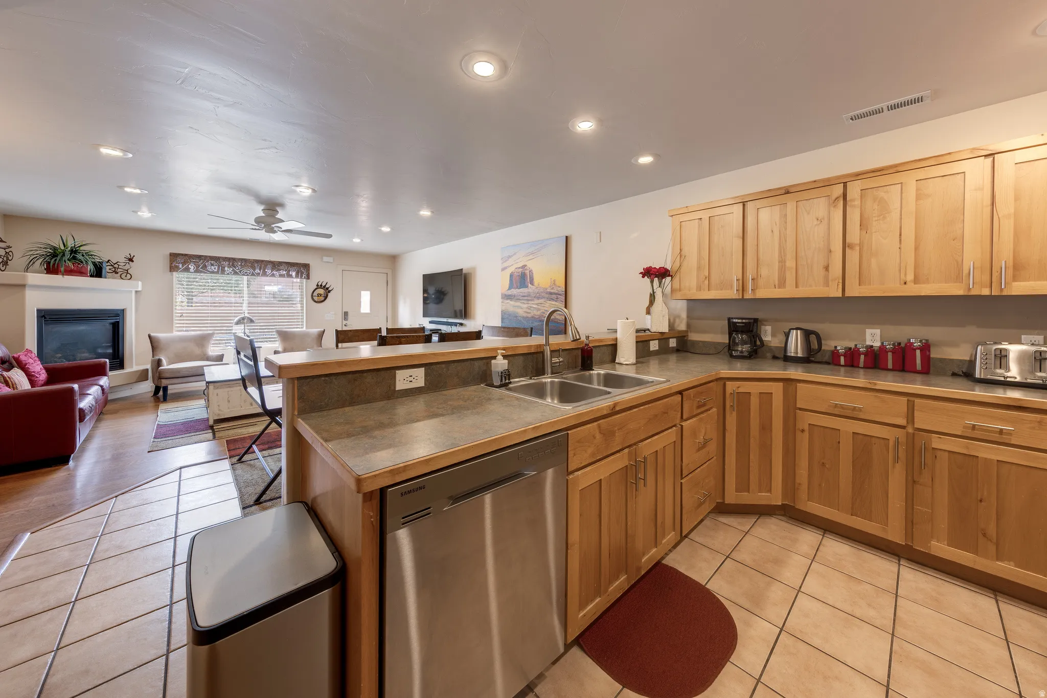 Kitchen featuring natural wood cabinetry, stainless steel dishwasher, double basin sink, and tile flooring
