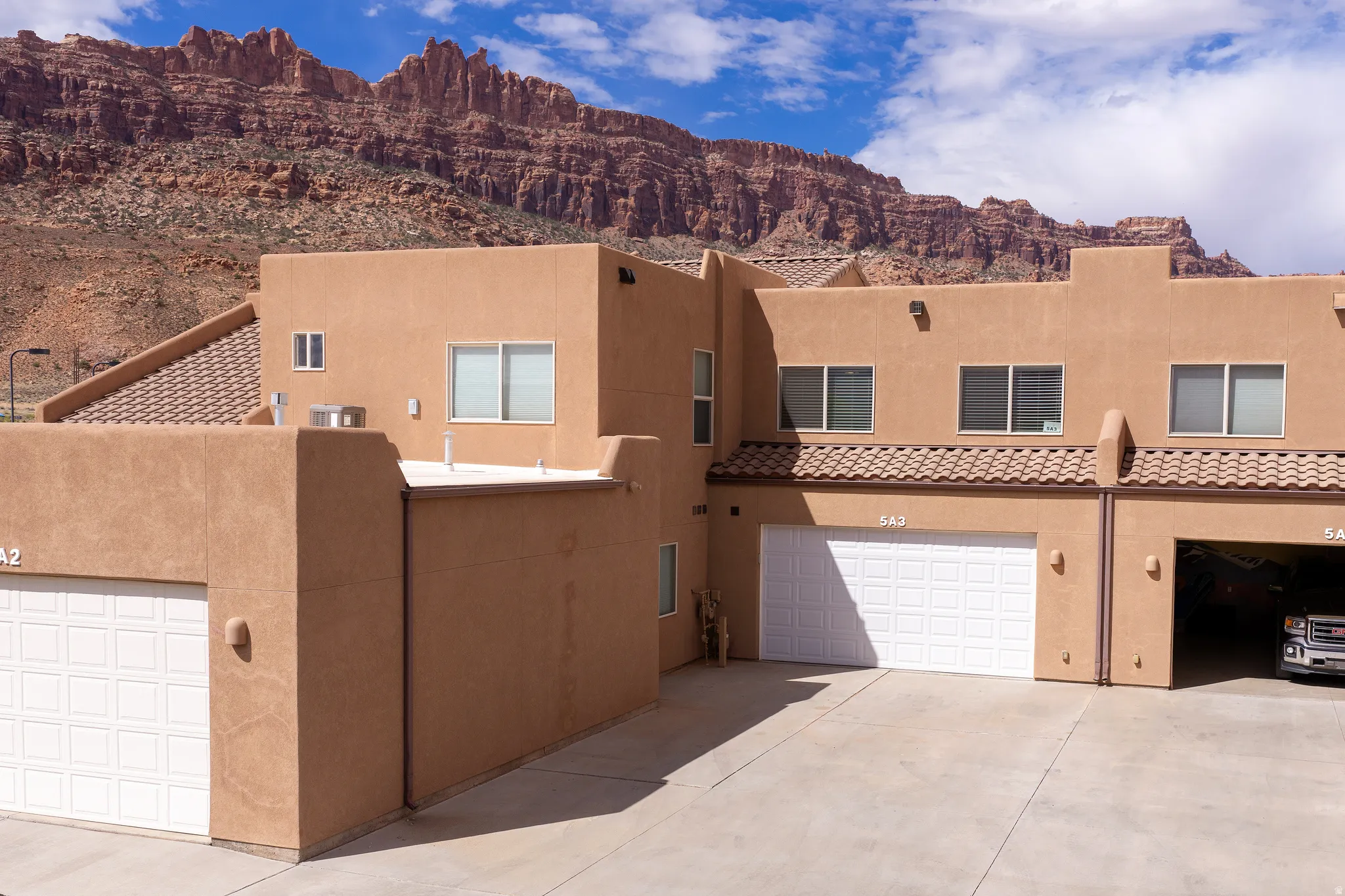Stucco exterior with multiple attached garages, tile roof accents, and a distinctive mountain backdrop