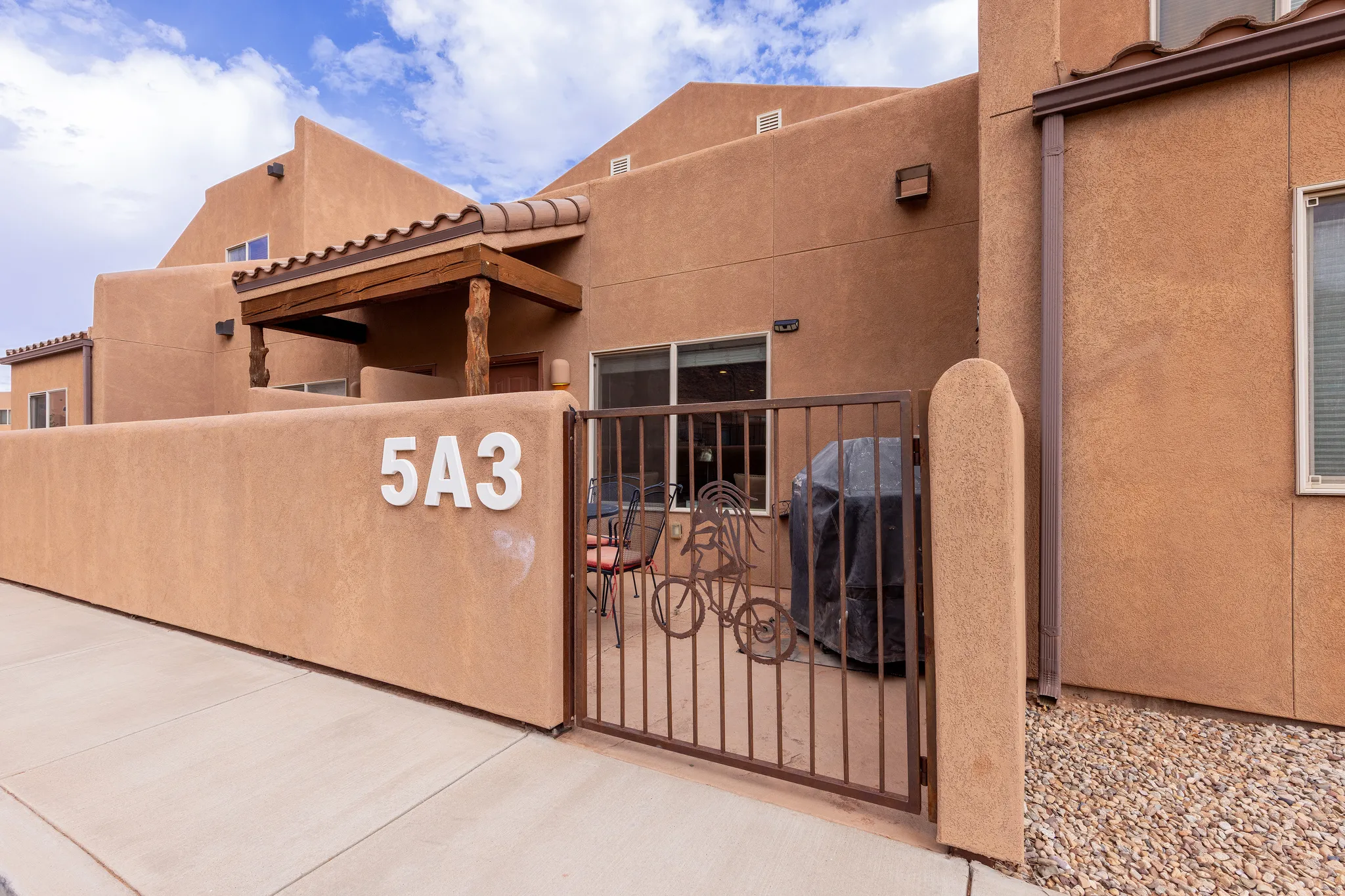 Stucco exterior with a tiled entry roof, exposed wood beams, and a private enclosed patio featuring a decorative metal gate
