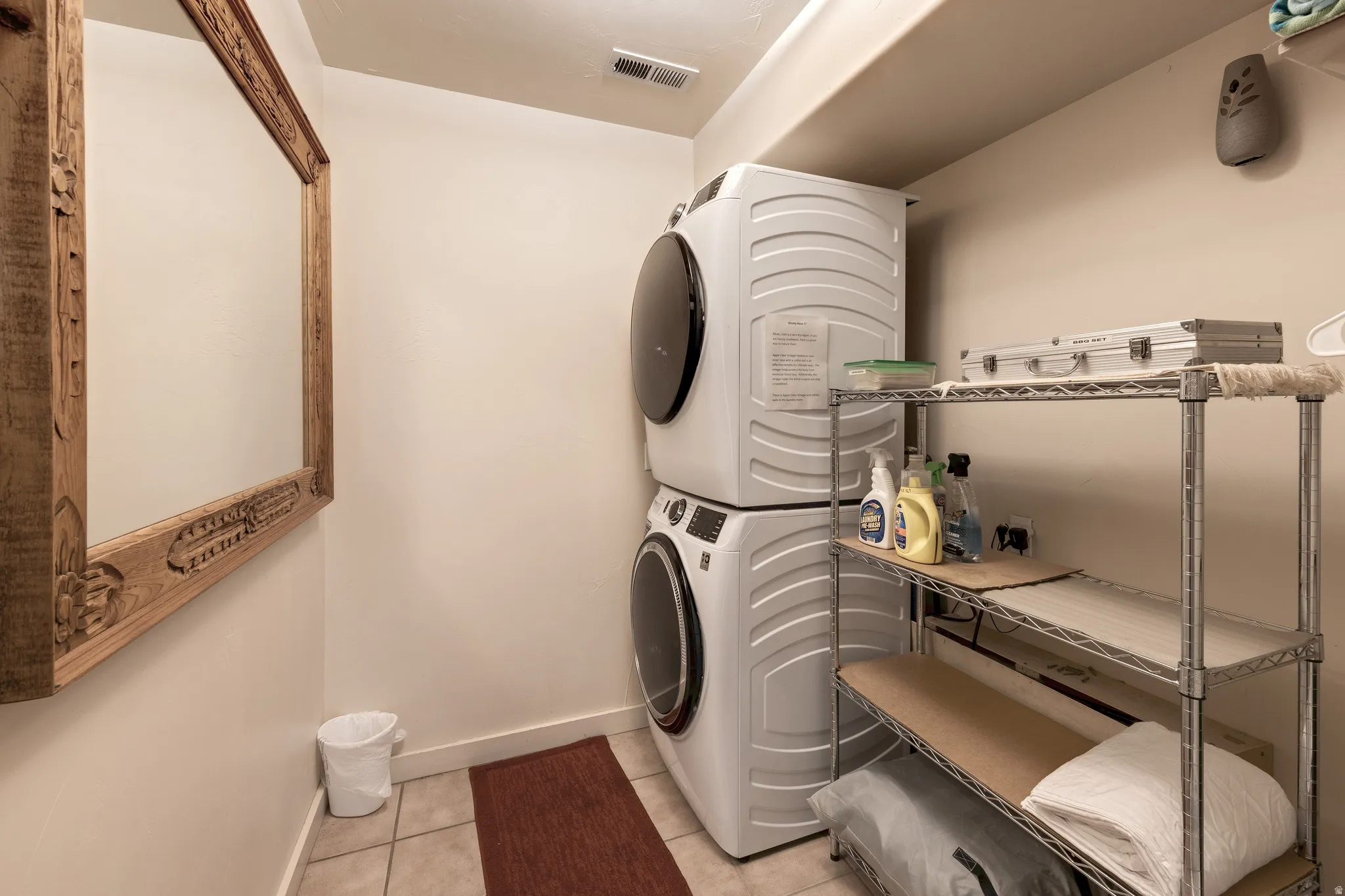Tile flooring, stacked laundry appliances, and built-in shelving