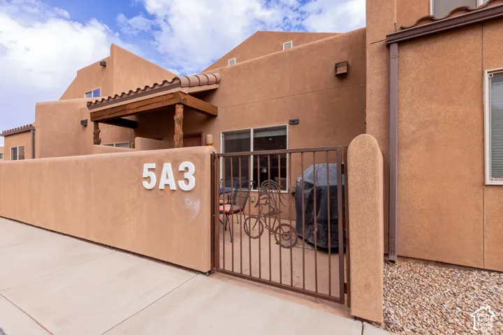 Stucco exterior with a tiled entry roof, exposed wood beams, and a private enclosed patio featuring a decorative metal gate