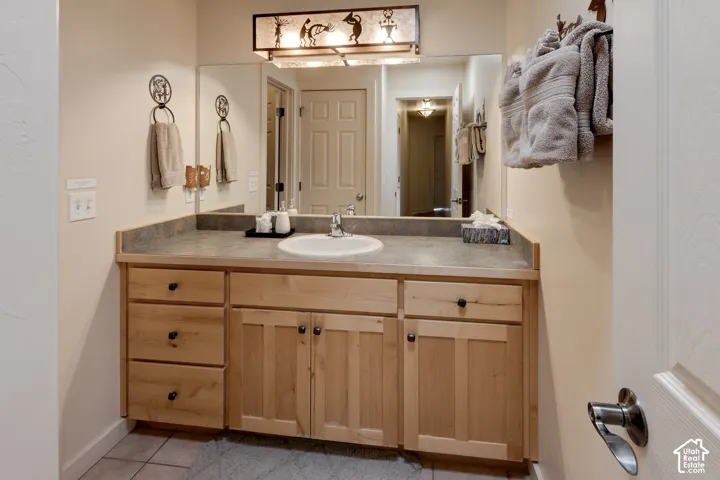 Light-toned vanity with wood-finish cabinetry, a single basin sink, and a dark countertop