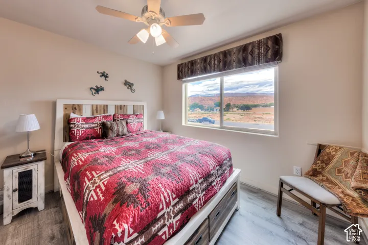 Bedroom featuring a rustic-style headboard, wood-finish flooring, and a ceiling fan with integrated lighting