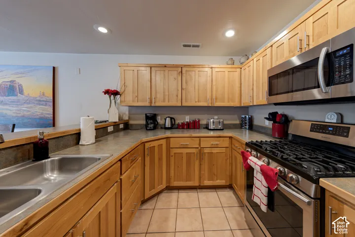U-shaped kitchen with wood cabinetry, stainless steel appliances, recessed lighting, and tile flooring