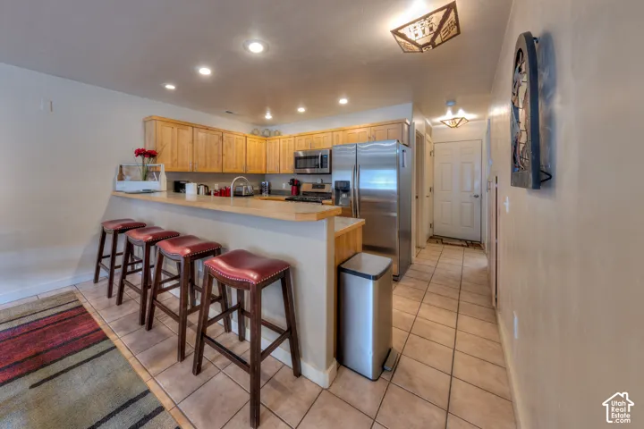 Kitchen featuring wood cabinetry, stainless steel appliances, a breakfast bar, recessed lighting, and tile flooring