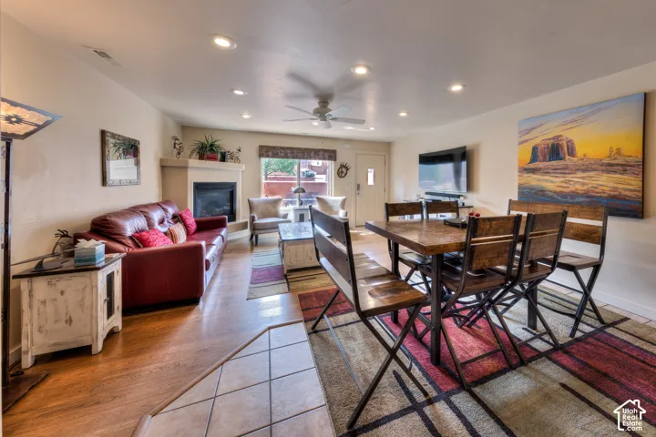 Corner fireplace with mantel, wood-finish flooring, recessed lighting, ceiling fan, and tiled entry