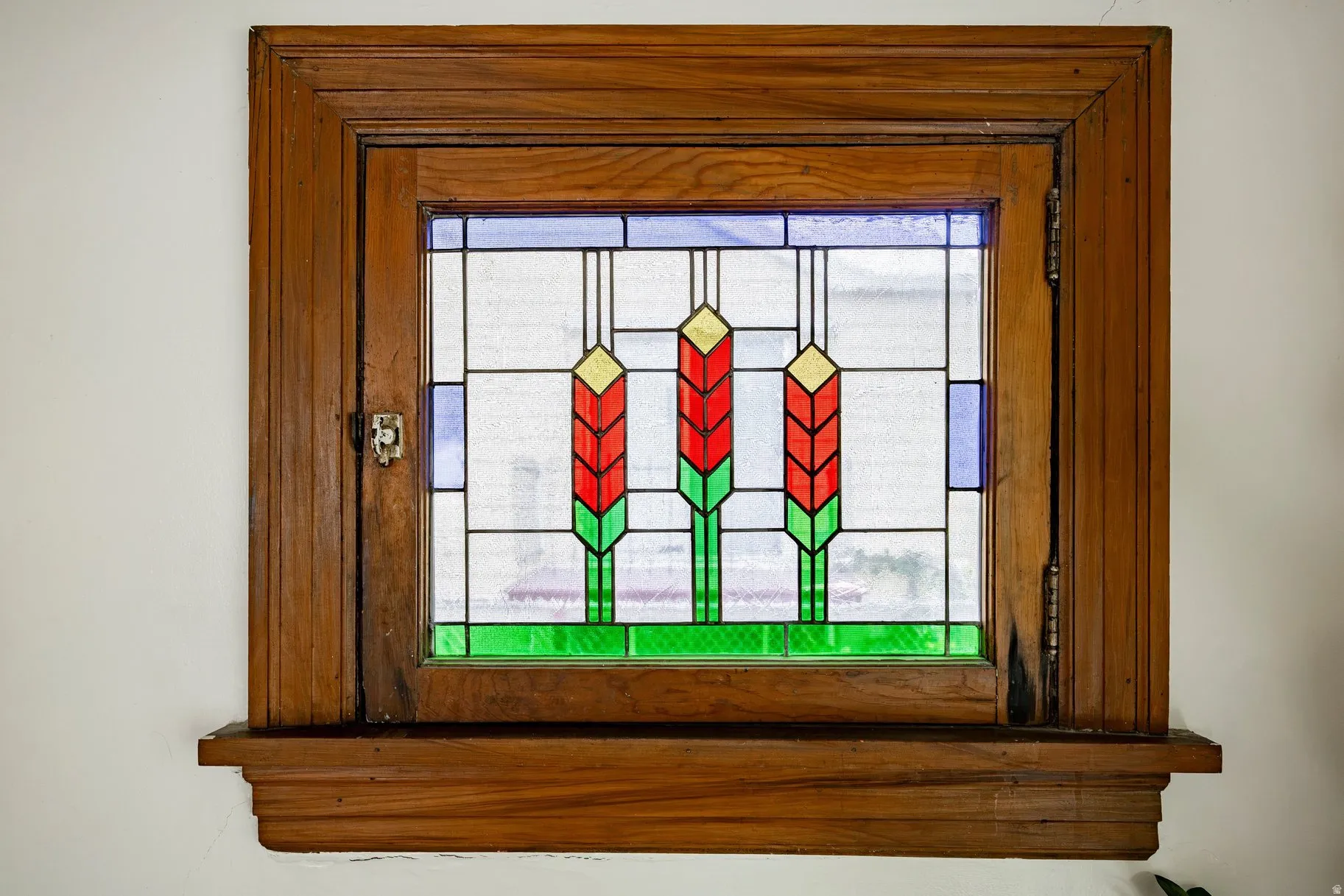 Stained glass window with intricate geometric and floral patterns, set within a rich wood frame and a decorative sill