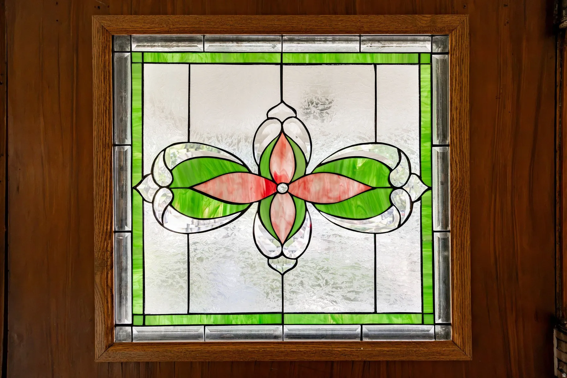 Stained glass window with a floral pattern, framed by a light wood trim and vertical wood paneling