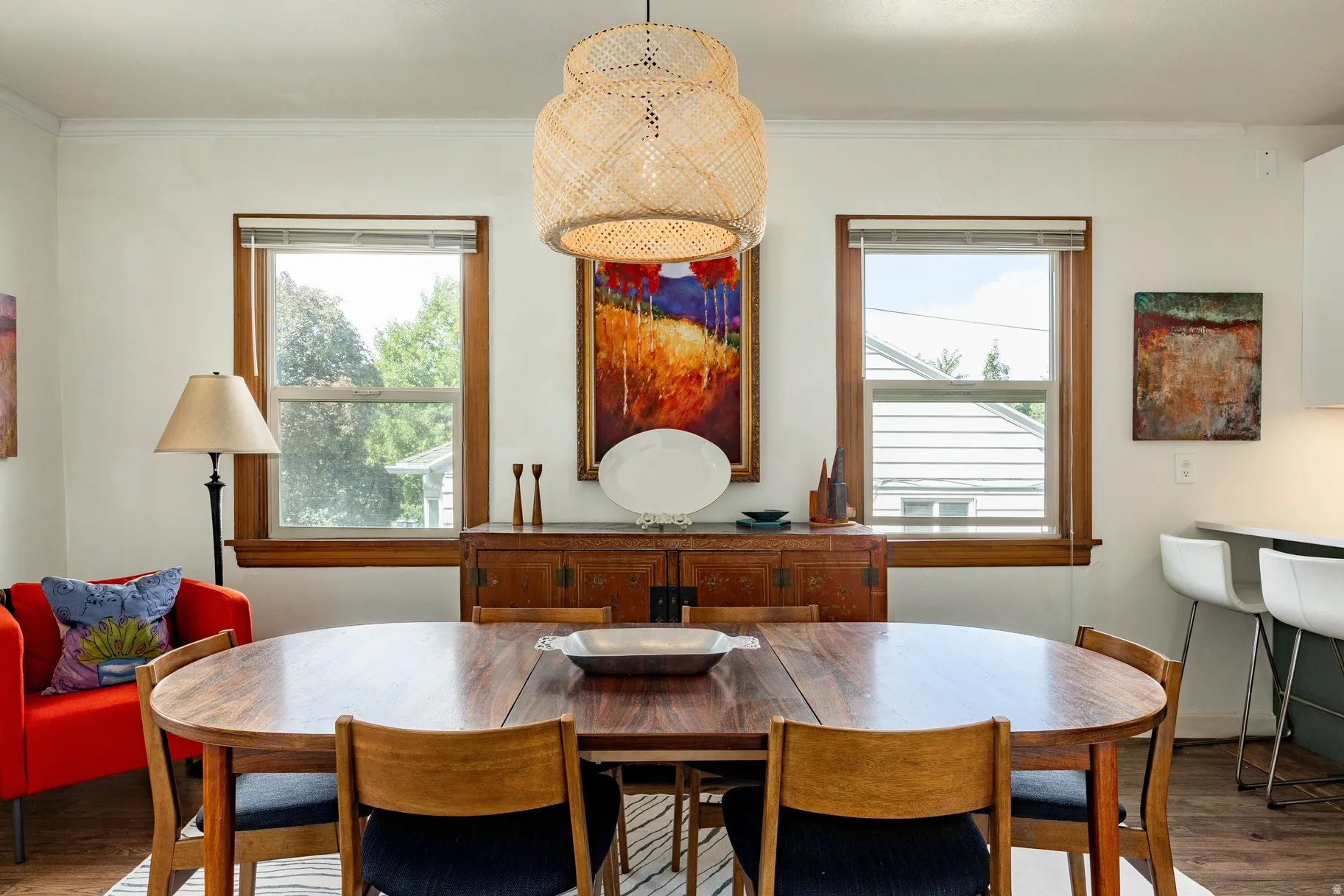 Dining area featuring a woven pendant light fixture, wood-finish flooring, and multiple windows with wood trim