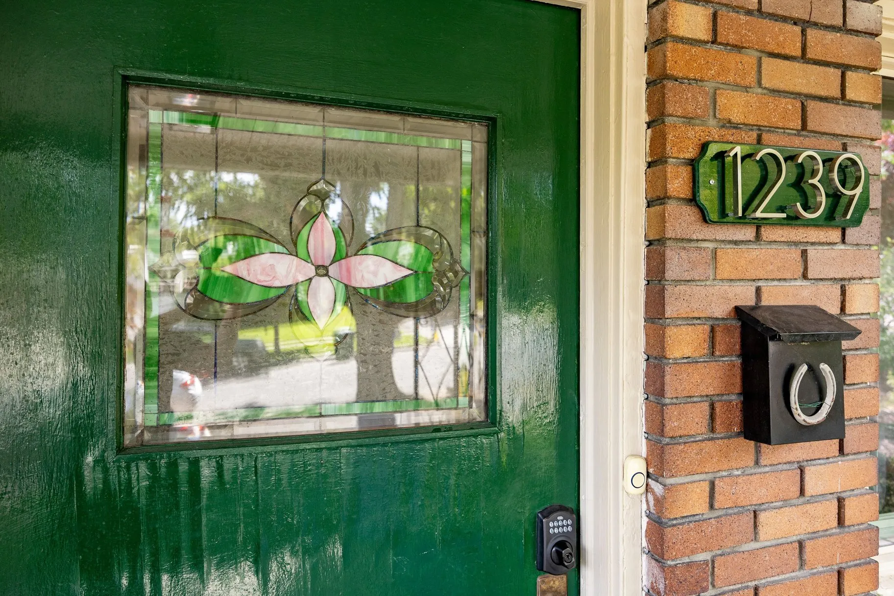 Green entry door with decorative stained glass, brick column detailing, and a wall-mounted mailbox