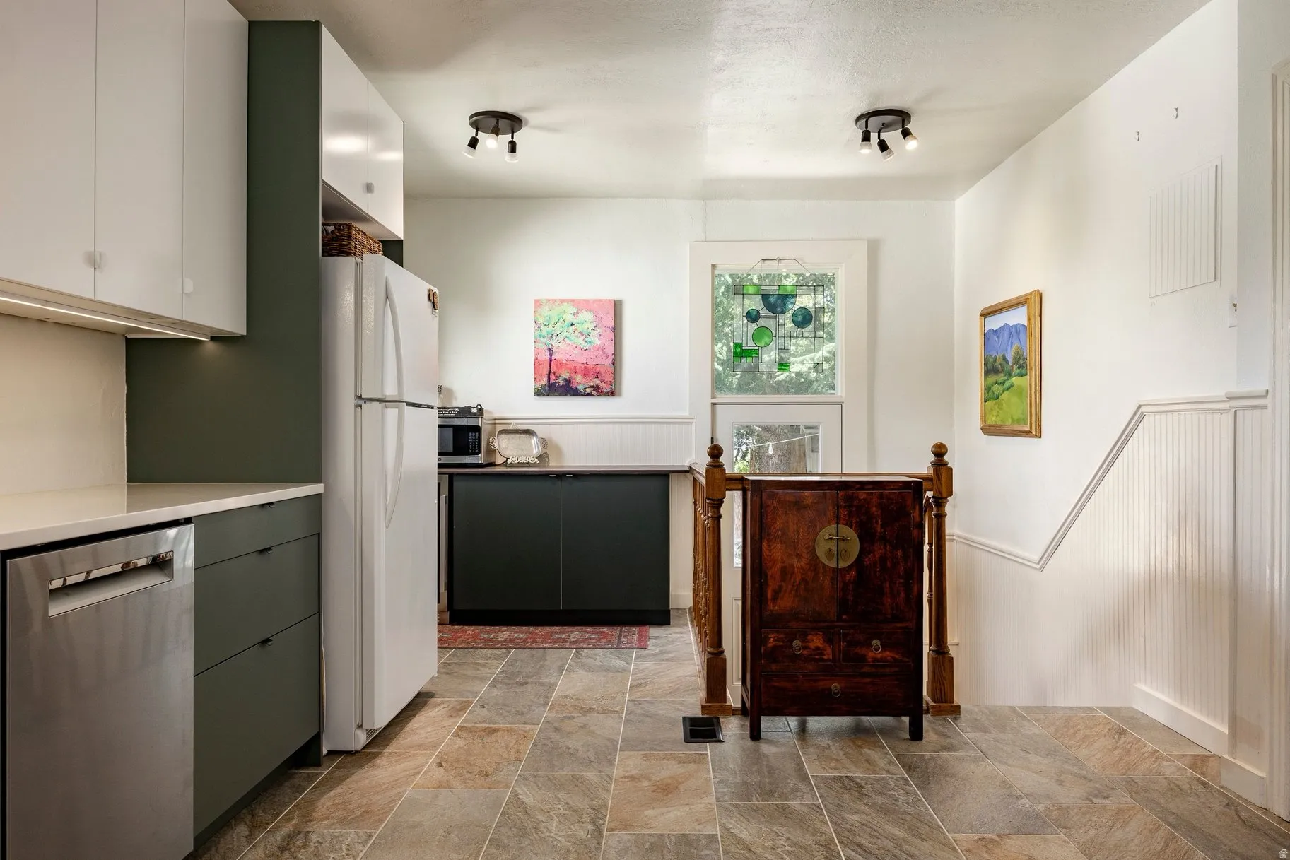Kitchen with stone-finish flooring, white upper cabinetry, dark lower cabinetry, and stainless steel dishwasher