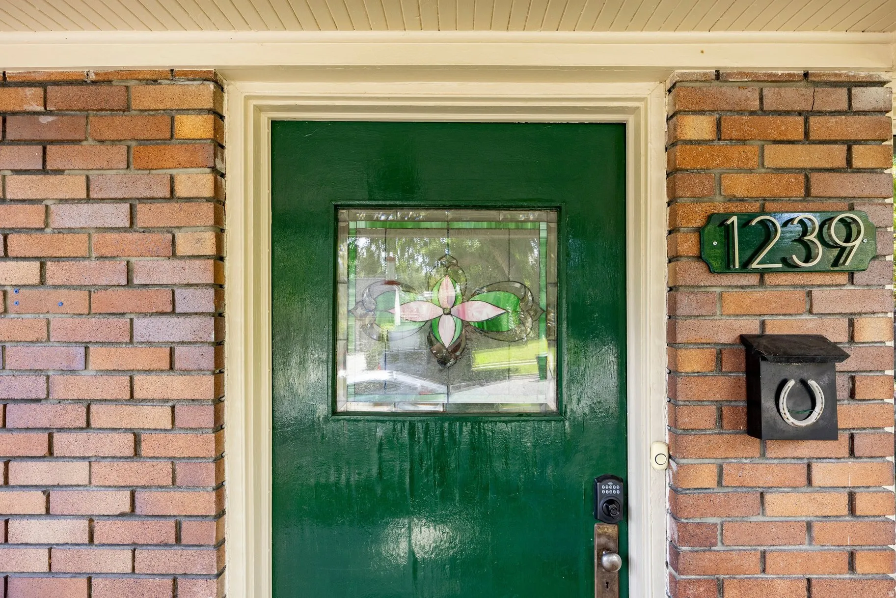 Brick exterior featuring a green entry door with decorative glass, a numerical address plaque, and a black mailbox