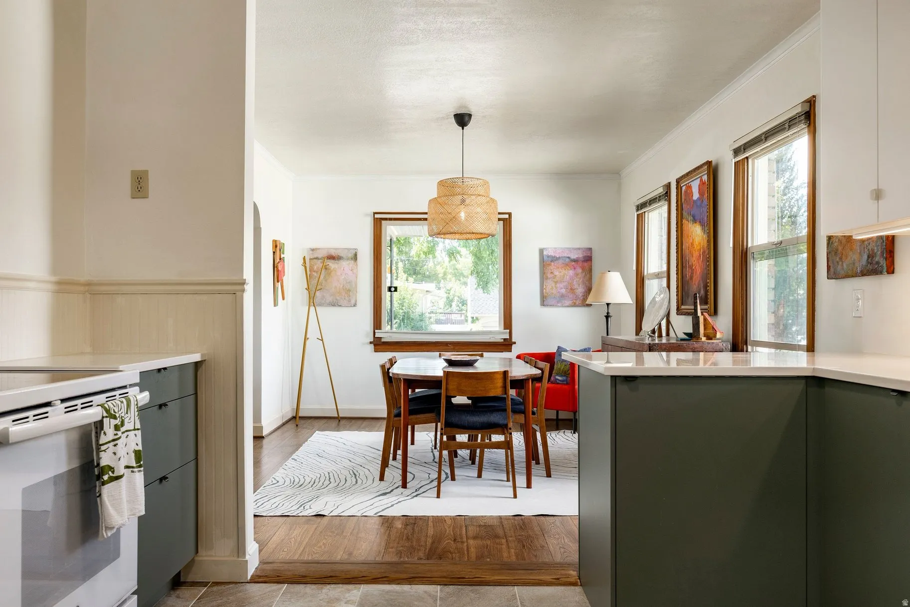 White countertops and dark green cabinetry in the kitchen, with wood-finish flooring extending into the dining area