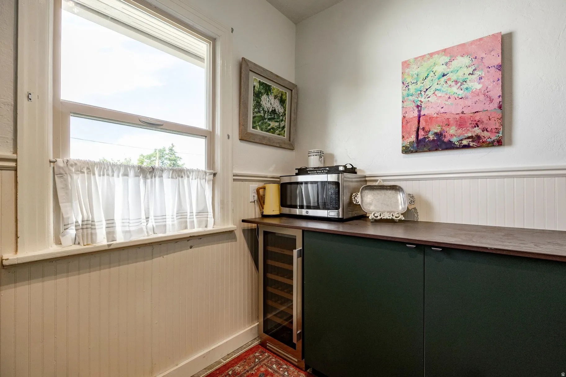 Built-in beverage cooler, wood-finish countertop, dark-finish cabinetry, beadboard wall paneling, and a large window