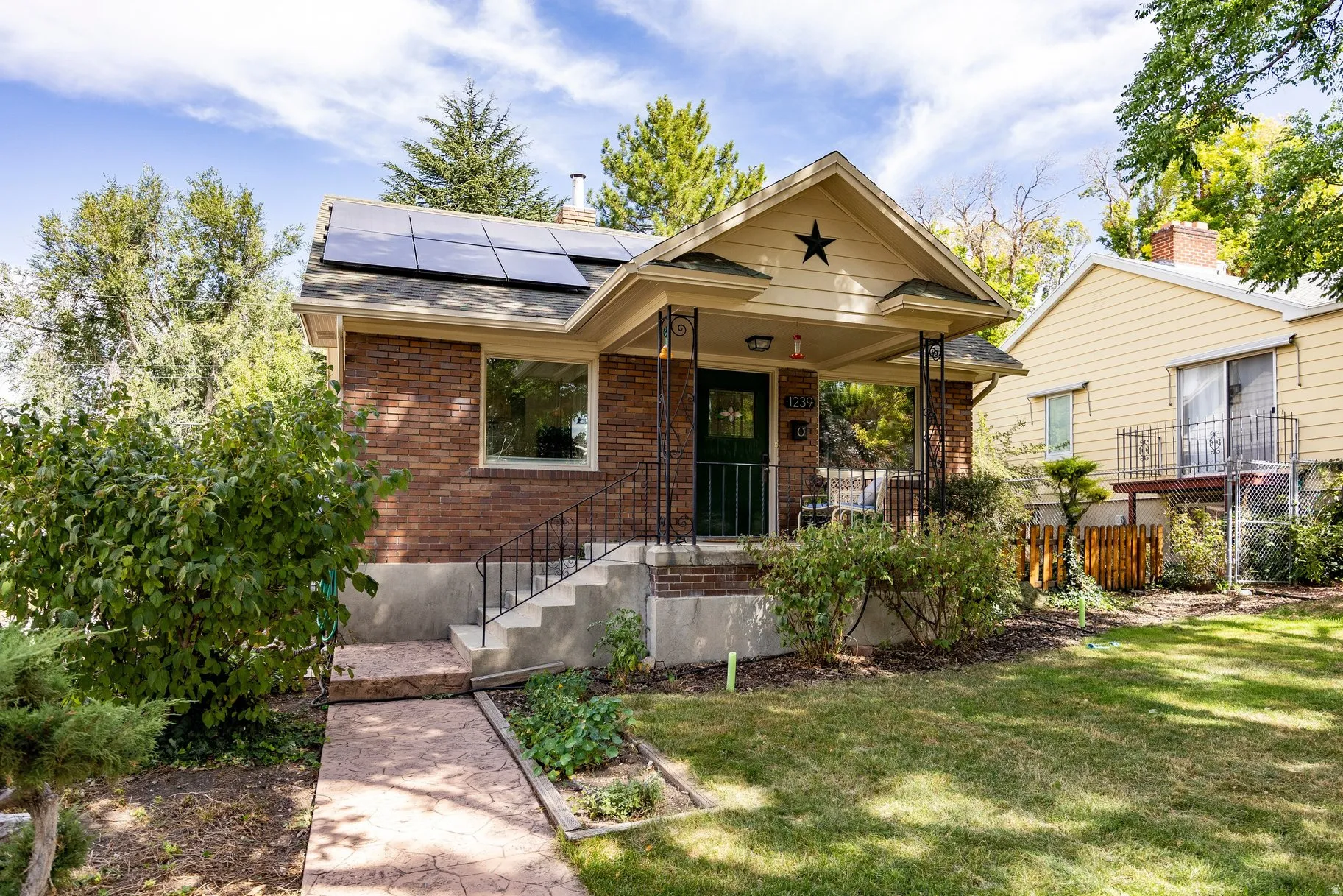 Brick exterior with solar panels, covered porch, concrete steps with wrought iron railing, and a patterned concrete walkway