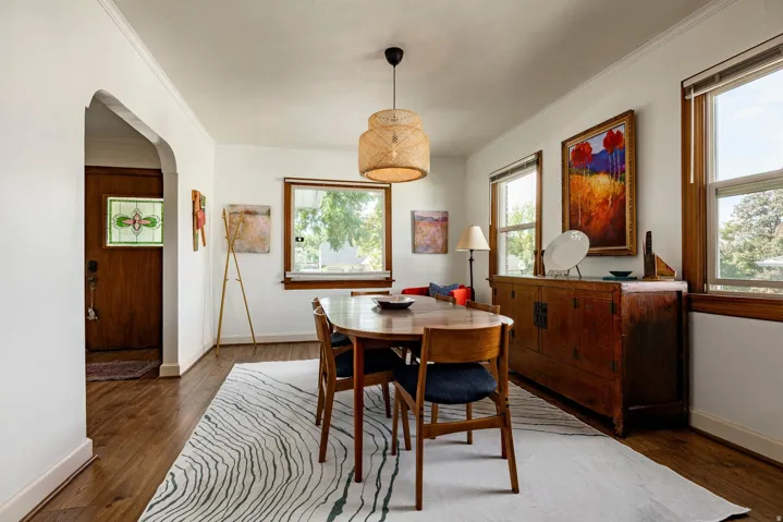 Wood-finish flooring, white wall paint, trim molding, arched doorway, and multiple windows