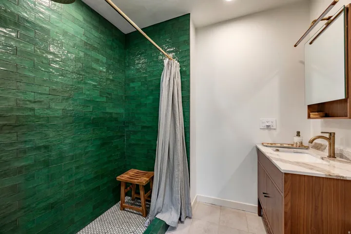 Green subway tile shower, white penny tile shower floor, wood-finish vanity with countertop, undermount sink, and wall-mounted faucet