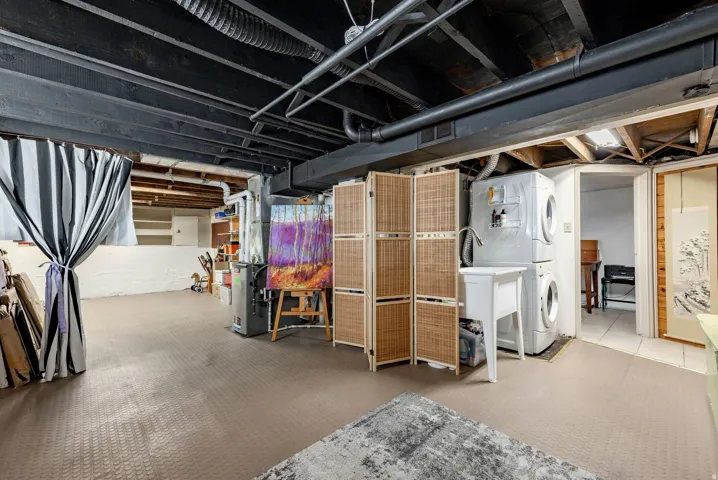 Expansive utility space featuring painted exposed ceiling joists, durable flooring, a stacked washer and dryer, and a utility sink