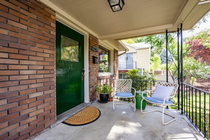 Covered front porch featuring a brick exterior, wrought iron railing, and a vibrant green entry door with a decorative glass insert