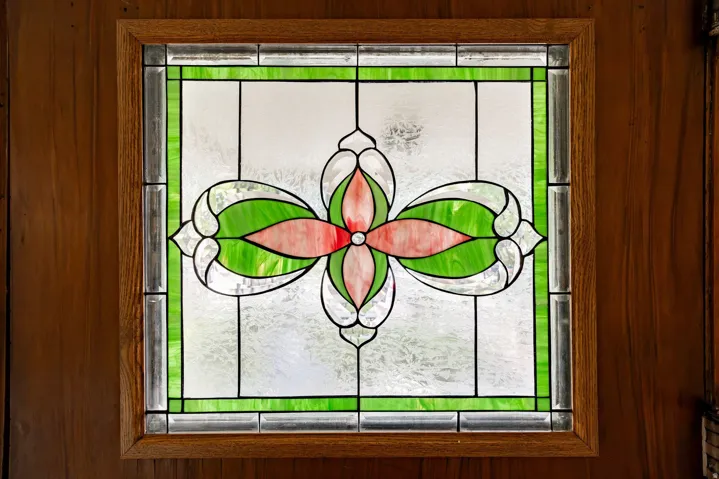 Stained glass window with a floral pattern, framed by a light wood trim and vertical wood paneling