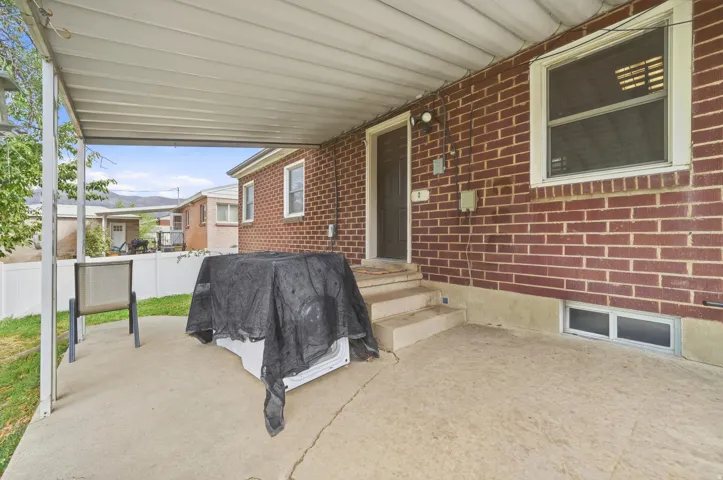 Covered concrete patio with a red brick exterior, white window trim, and a privacy fence