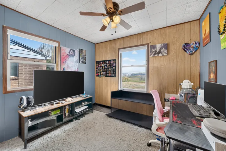 Wood-finish paneled wall, blue-painted paneling, drop ceiling with ceiling fan, and two windows providing natural illumination