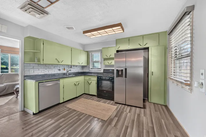 Kitchen featuring wood-finish flooring, light green cabinetry, stainless steel refrigerator, stainless steel dishwasher, and a white subway tile backsplash
