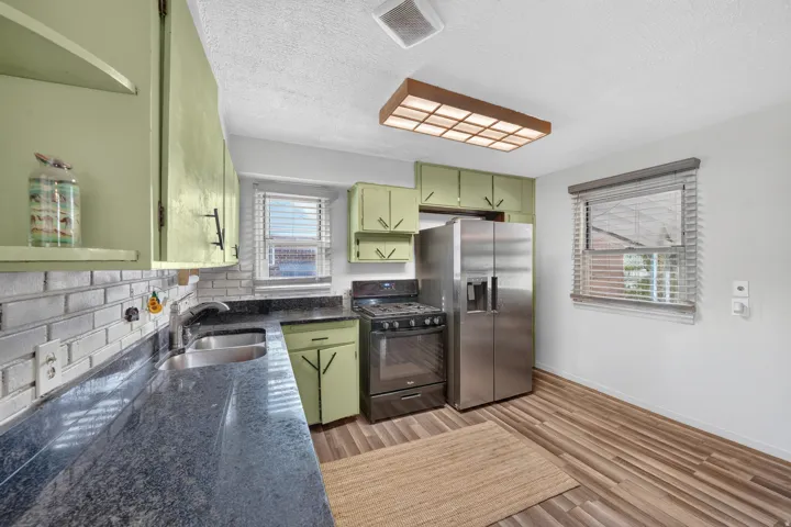 Kitchen featuring wood-finish flooring, light green cabinetry, dark countertops, a tile backsplash, and stainless steel appliances
