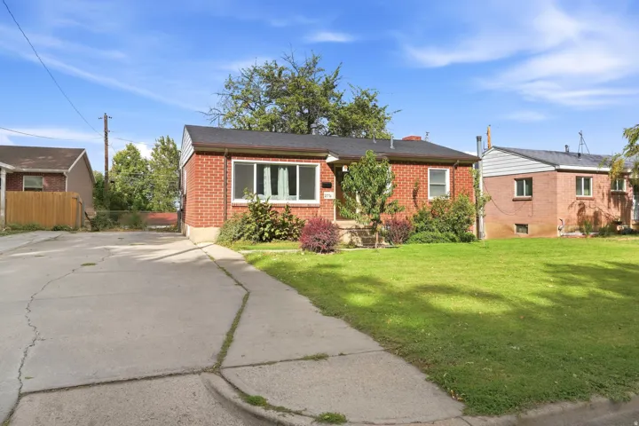 Brick exterior with a dark shingle roof, concrete driveway, and front lawn