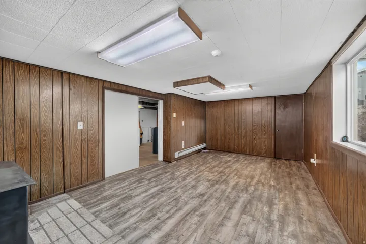 Wood-finish paneling, drop ceiling with recessed lighting, wood-finish flooring, and a sliding door entrance