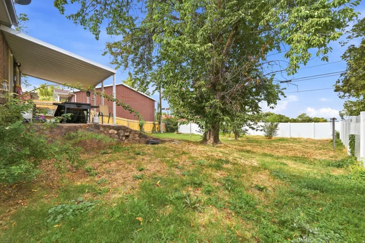 Covered patio with a stone retaining wall and a spacious rear yard featuring mature trees and white fencing