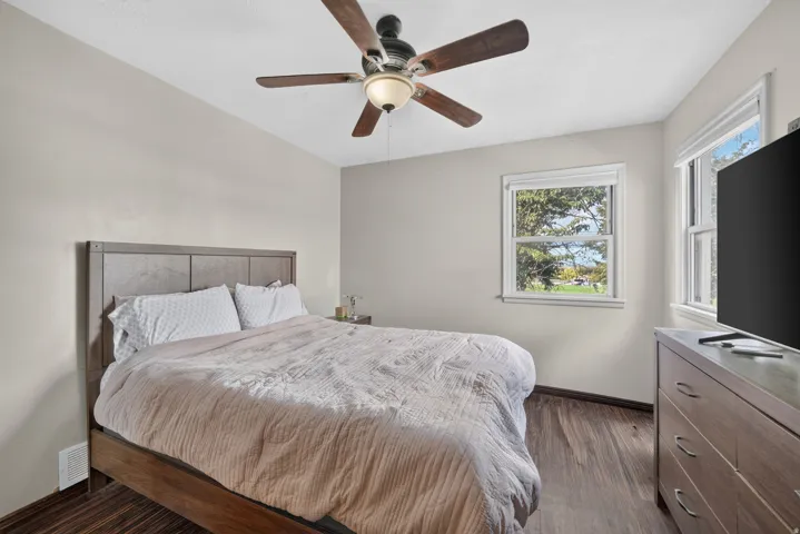 Wood-finish flooring, ceiling fan with integrated lighting, and multiple windows providing natural illumination