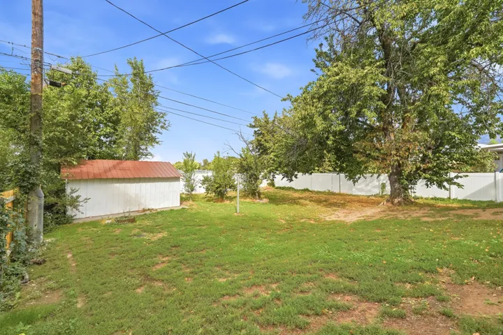 Expansive backyard featuring a mature tree, a white storage shed with a red roof, and a white privacy fence