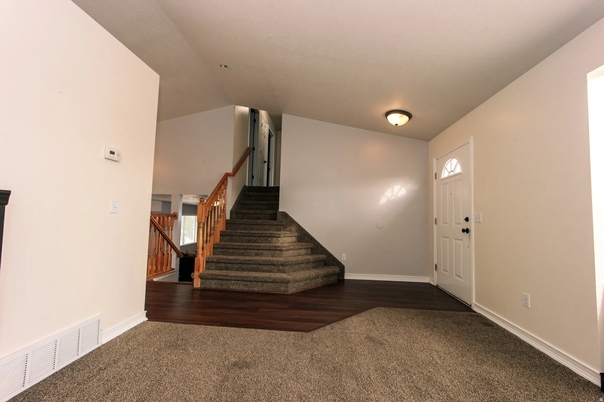 Carpeted flooring, wood-finish flooring, staircase with wood railing, recessed entry, and wall-mounted lighting