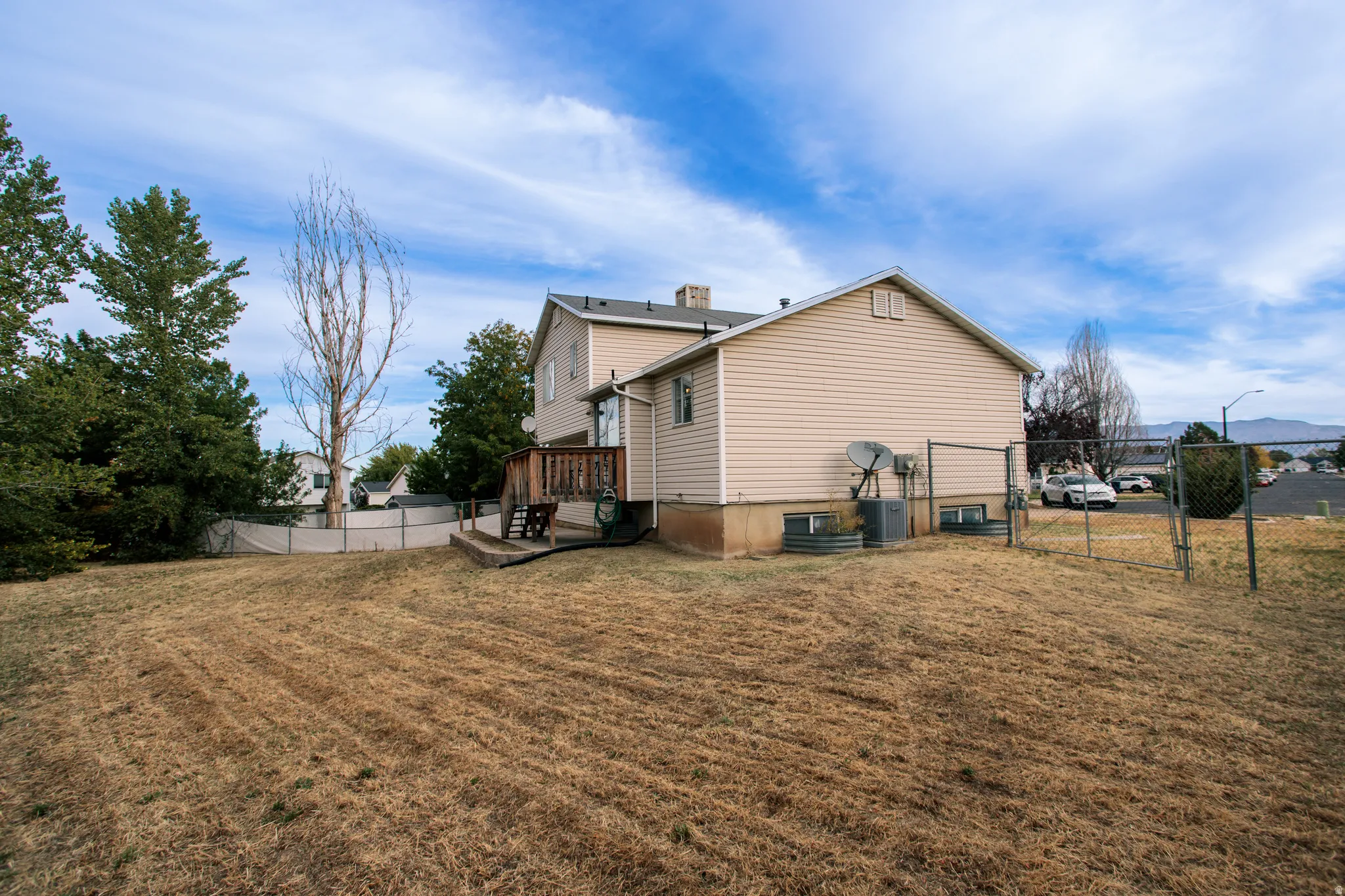 Expansive backyard featuring a chain-link fence, a multi-level wood deck, and mature trees