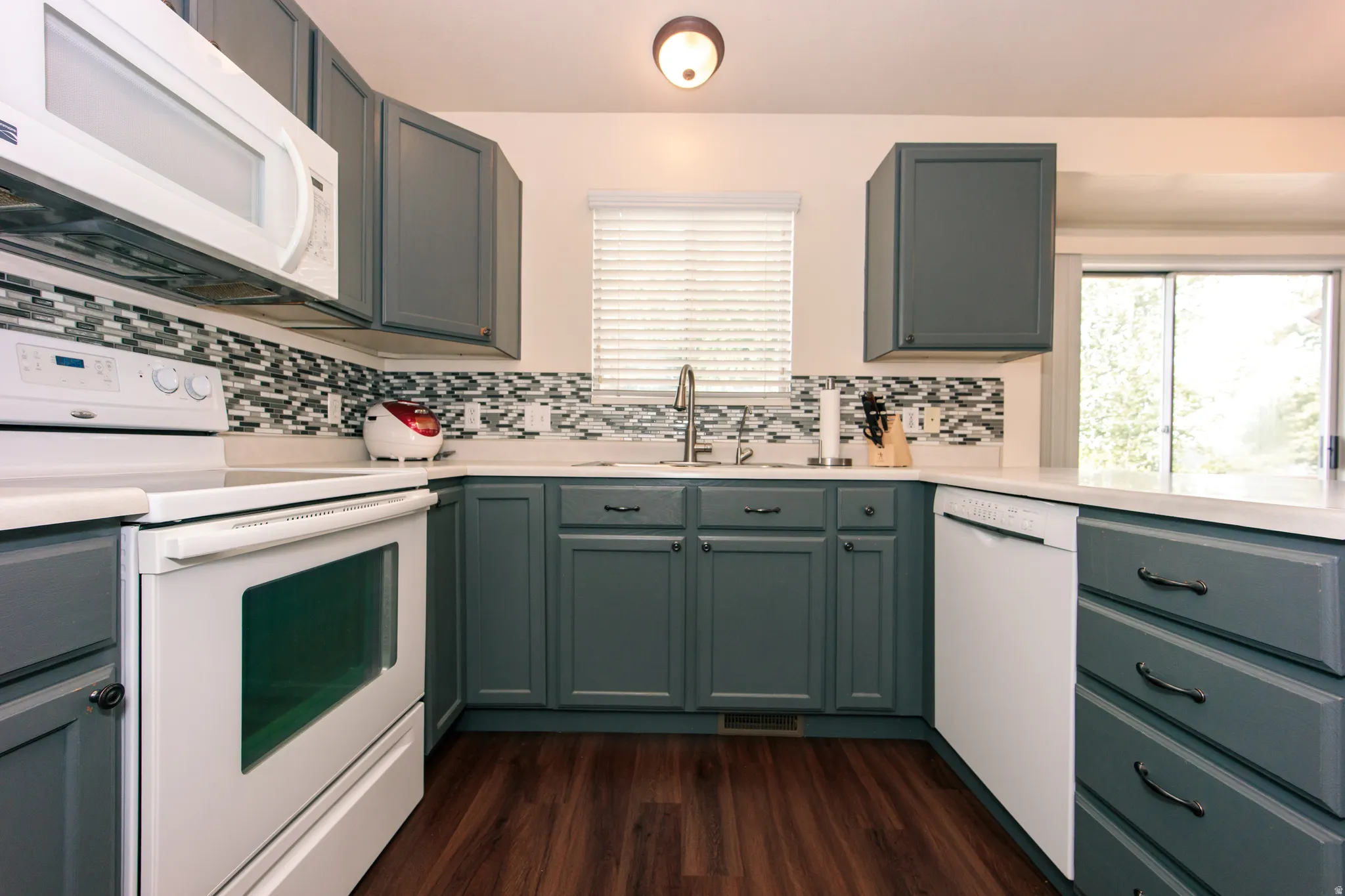 Kitchen featuring dark gray cabinetry, white countertops, a mosaic tile backsplash, wood-finish flooring, and a sliding glass door