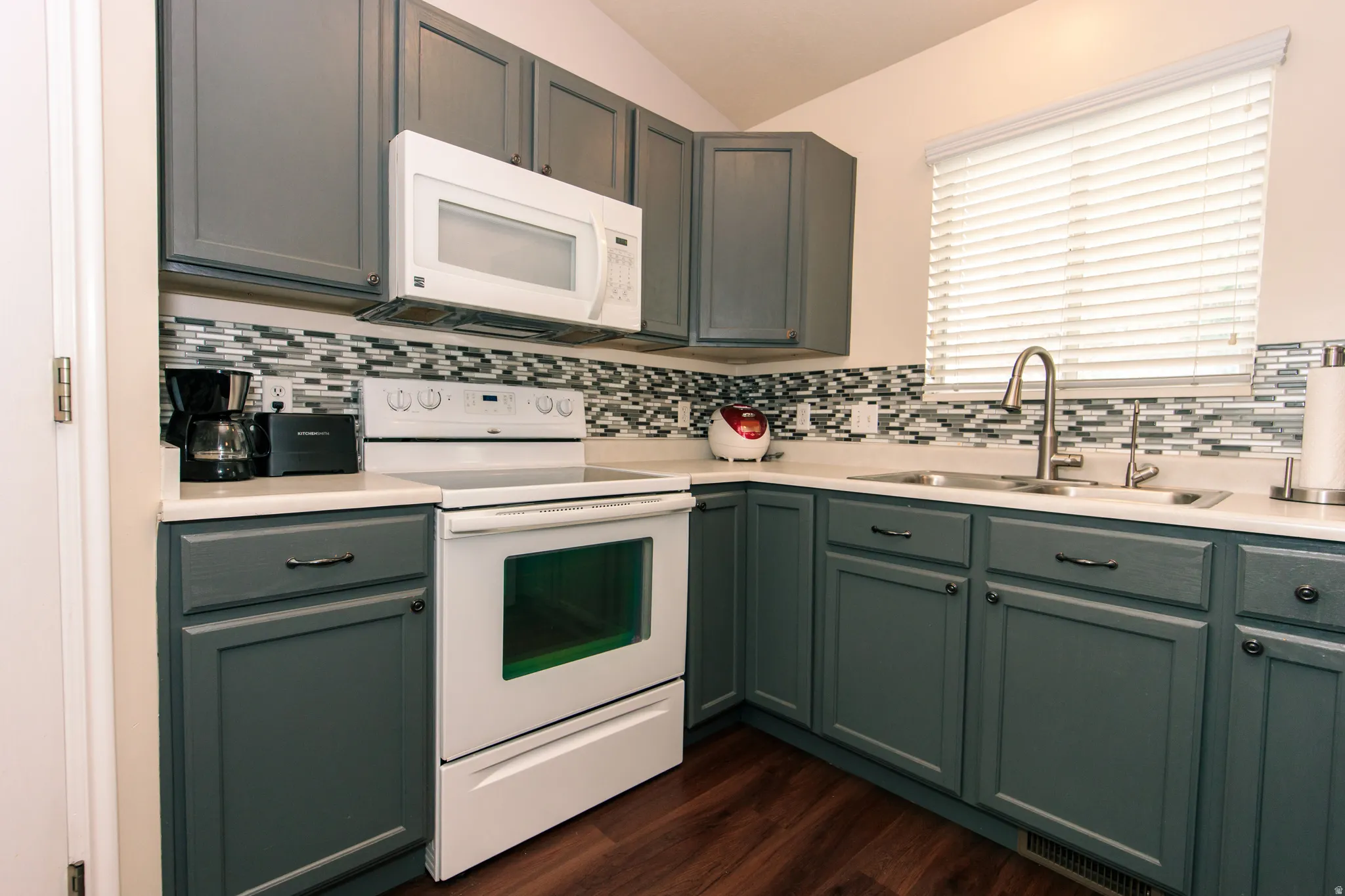Gray cabinetry with black hardware, white countertops, glass tile backsplash, and wood-finish flooring