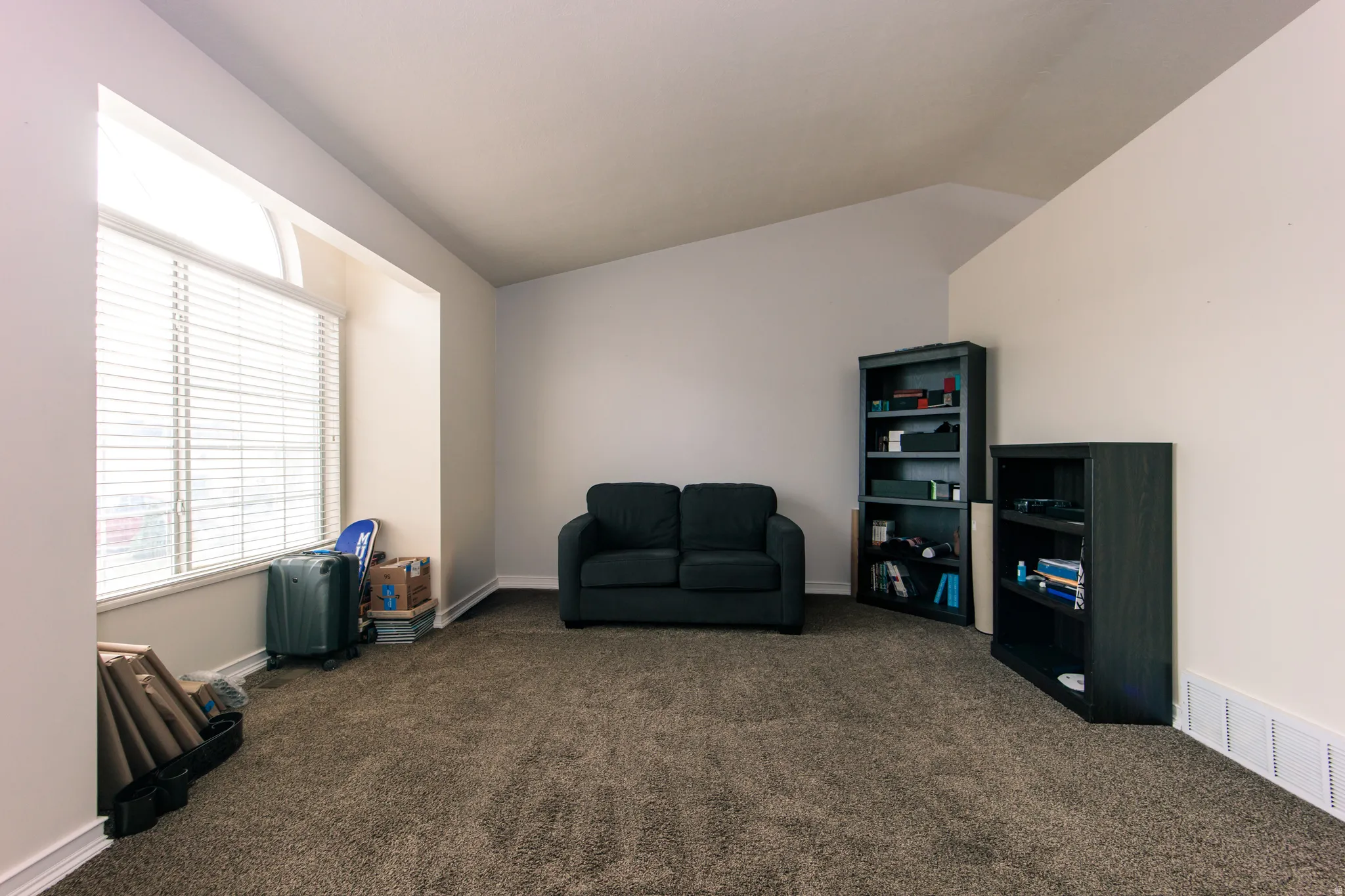Vaulted ceiling, carpeted flooring, and a large window with blinds
