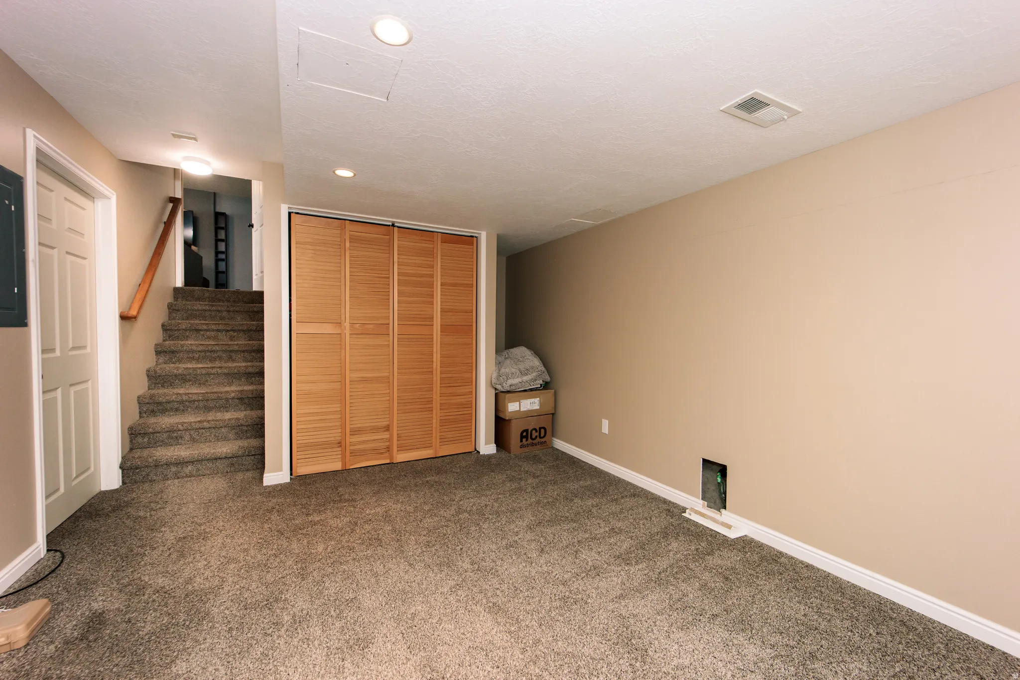 Carpeted flooring, neutral wall paint, recessed ceiling lighting, wood-finish bi-fold closet doors, and a carpeted staircase with wood handrail