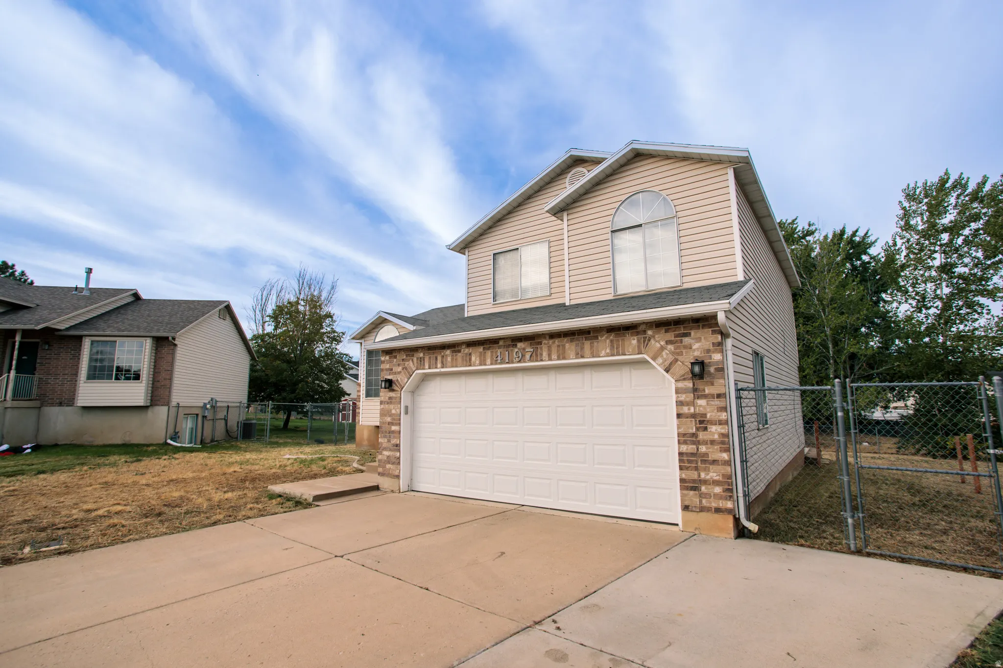 Two-story facade with brick and siding, arched window, attached garage, and paved driveway