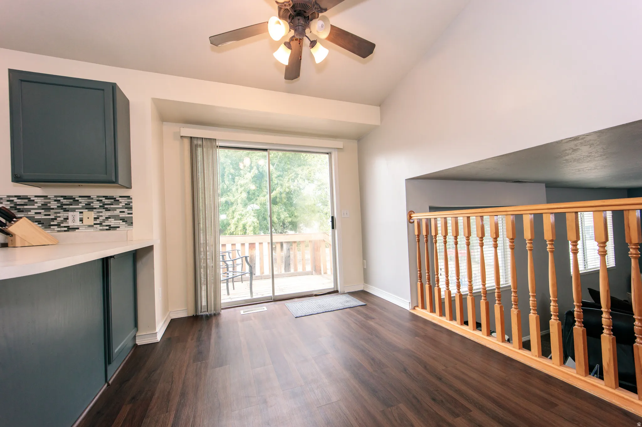Wood-finish flooring, vaulted ceiling, sliding glass door to exterior deck, wood balustrade, and contemporary cabinetry
