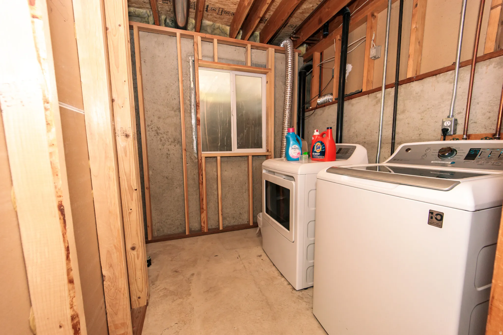 Unfinished basement space featuring exposed wood framing, concrete flooring, and a basement window