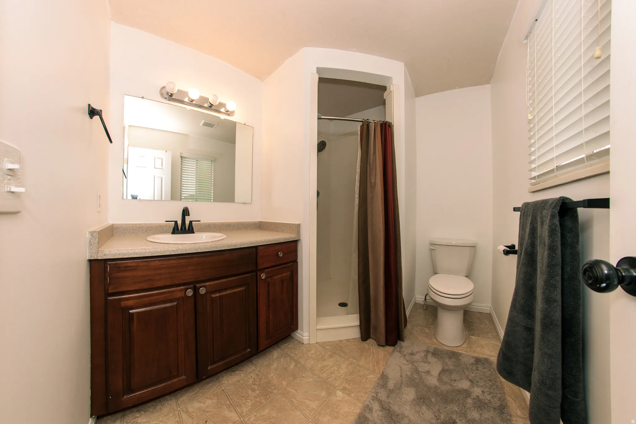 Spacious bathroom featuring a dark wood finish vanity with a light-toned countertop, an integrated sink with a matte black faucet, and a shower enclosure