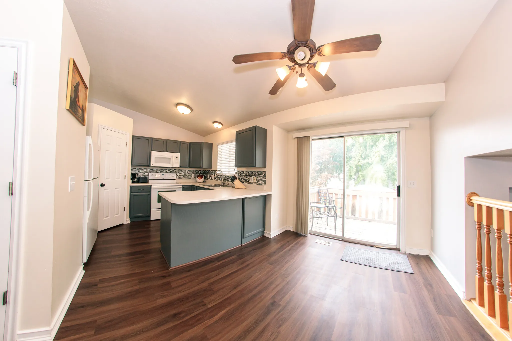 Vaulted ceiling kitchen featuring wood-finish flooring, white appliances, a sliding glass door, and a built-in kitchen island with countertop