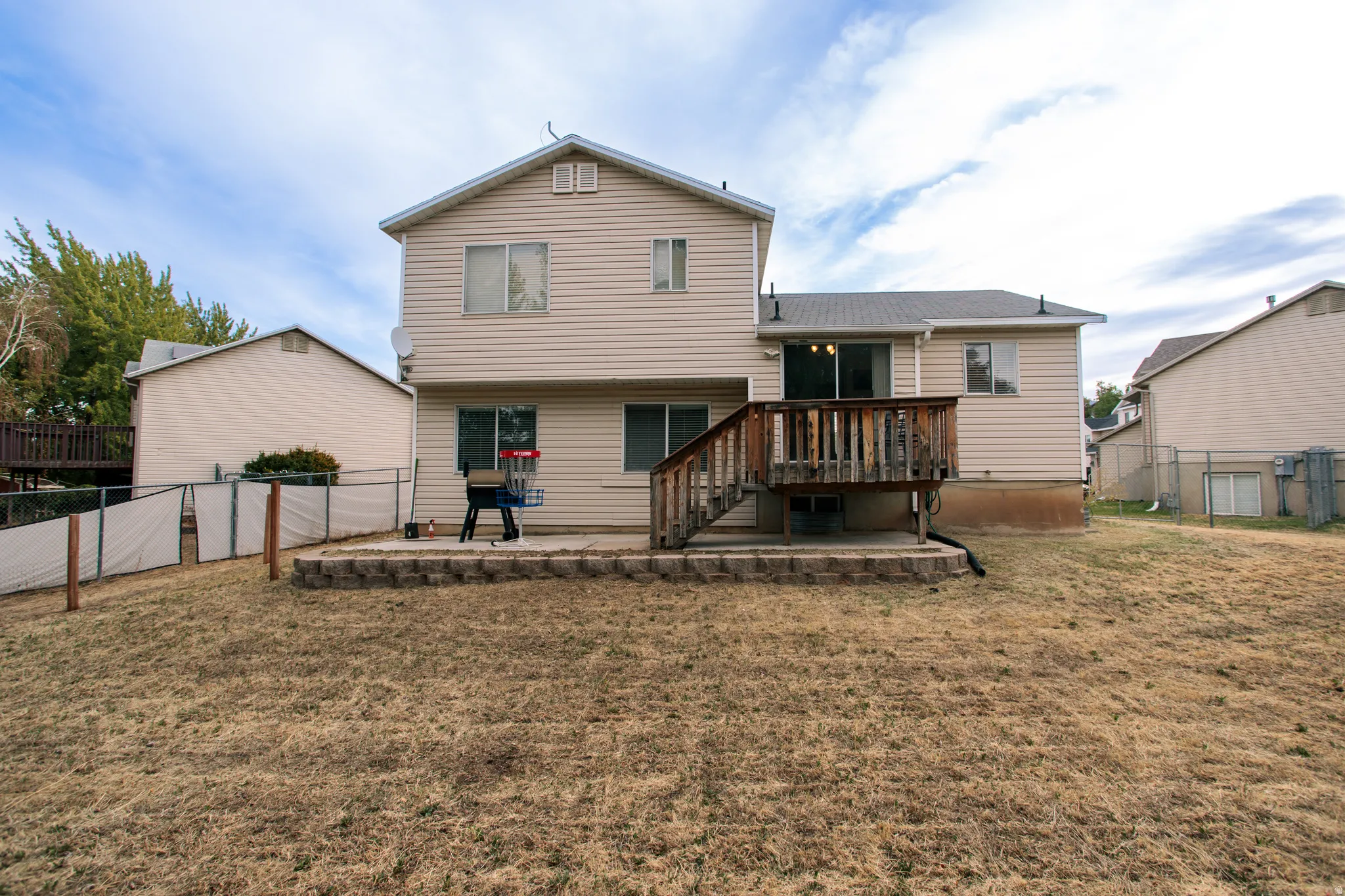 Rear exterior featuring a two-story design, siding facade, a raised wood deck with staircase, and a ground-level patio with a retaining wall